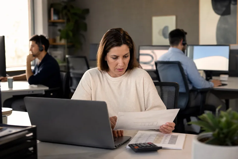 Sales operations manager reviewing a monthly CRM and calling invoice while two reps work the phones