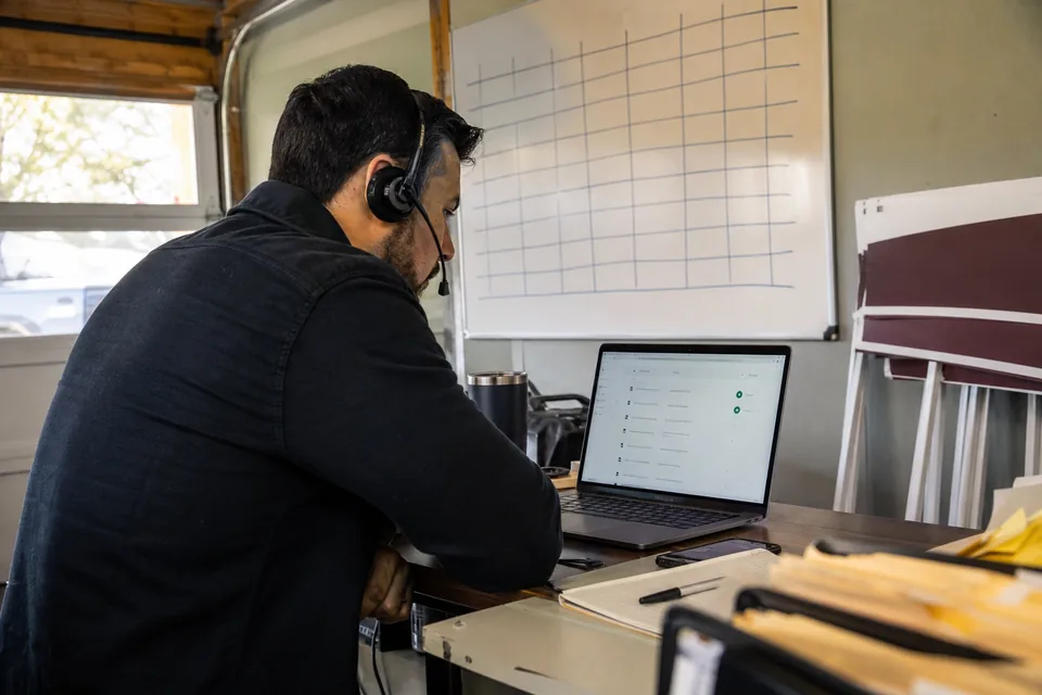Real estate team lead on a headset dialing a contact list from a small brokerage office